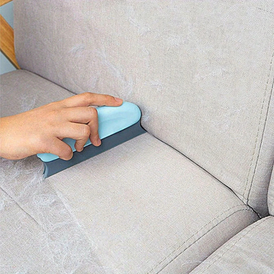 Person using a tool to clean a gray fabric sofa