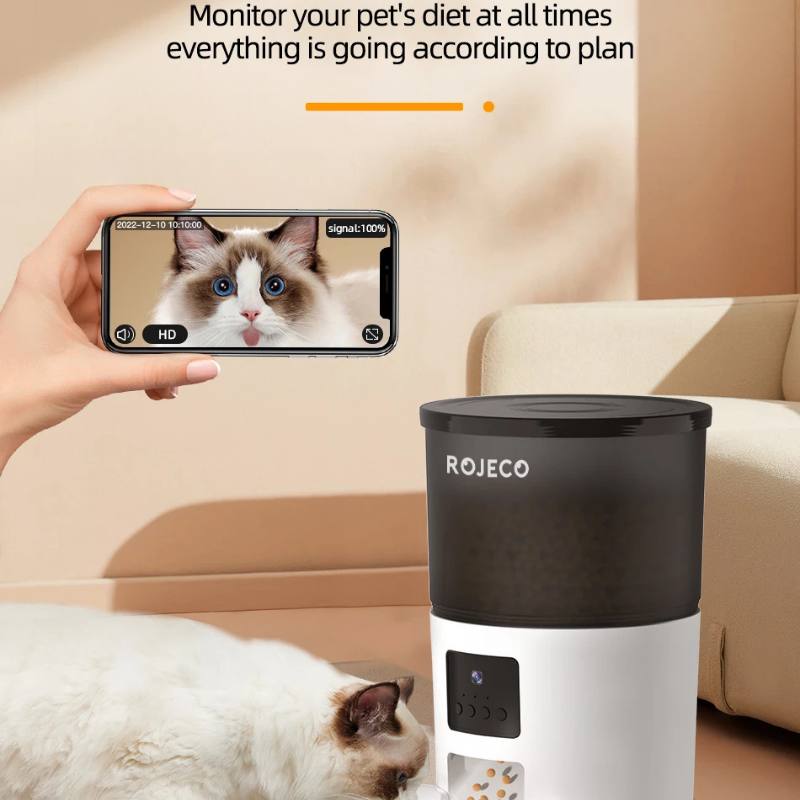 Person using a smartphone to monitor a cat with a ROJECO pet feeder in the background.