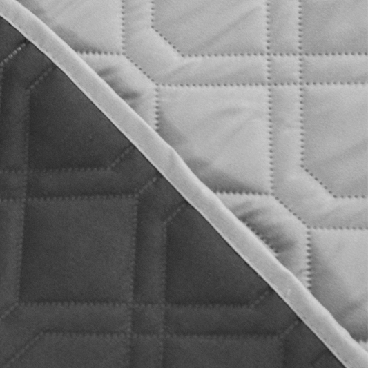 Close-up of a quilted fabric with a geometric pattern, showing a transition from gray to black.