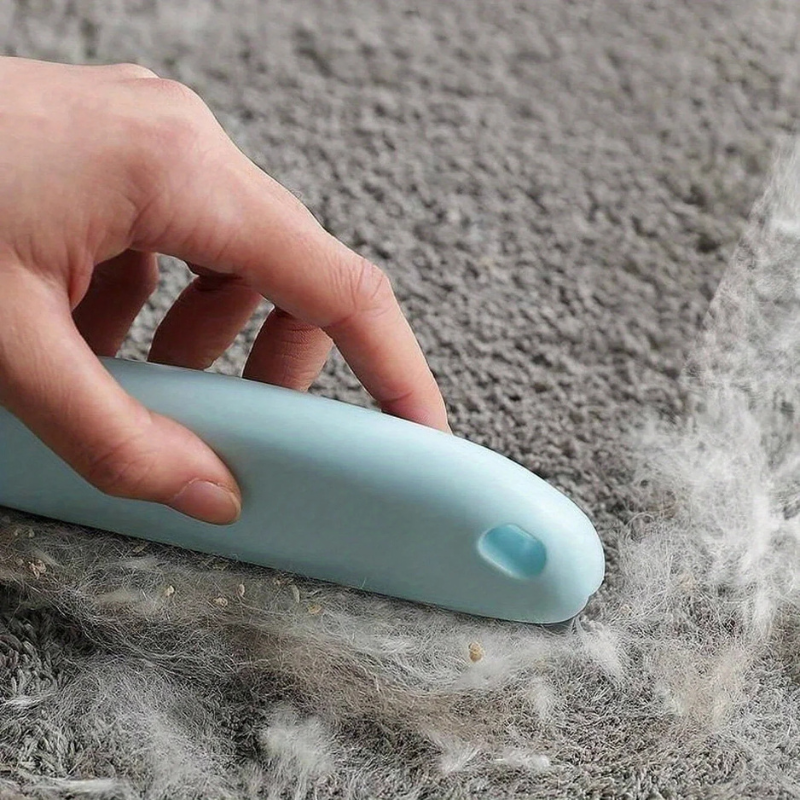 Hand using a blue tool to remove pet hair from a carpet