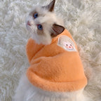 Cat wearing an orange outfit with a patch on a fluffy white surface