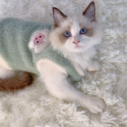 Kitten wearing a green sweater with a flower design on a fluffy white surface